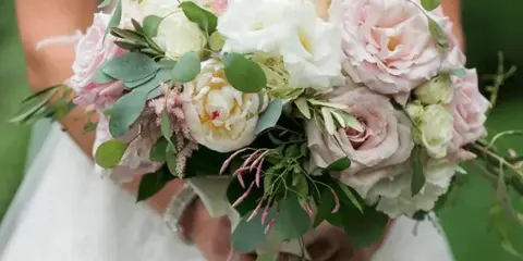 Bride holding a round wedding bouquet of white and blush roses with eucalyptus and pink filler flowers.