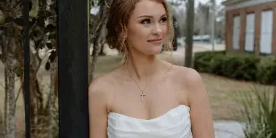 A bride in a white strapless gown holding a white floral bouquet, standing outdoors near a black iron gate.