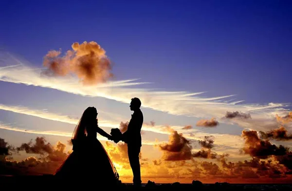Silhouette of a bride and groom holding hands during a wedding ceremony at sunset.