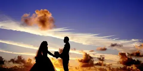 Silhouette of a bride and groom holding hands during a wedding ceremony at sunset.