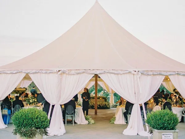A large white event tent with draped fabric and set tables at a wedding reception.