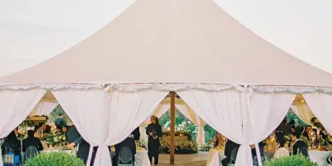 A large white event tent with draped fabric and set tables at a wedding reception.