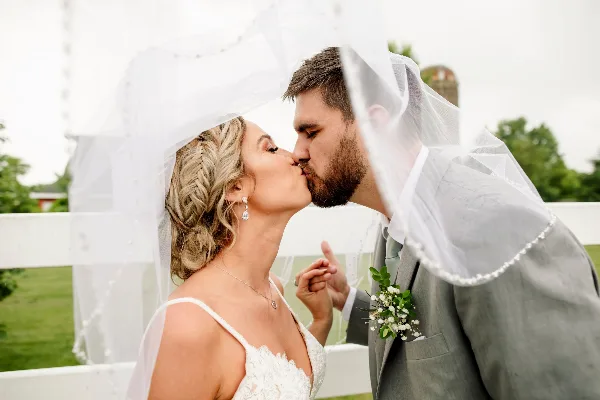 A bride and groom kissing under a veil in a wedding photograph.