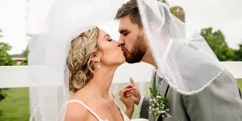 A bride and groom kissing under a veil in a wedding photograph.