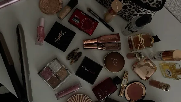 A flat-lay photograph of various professional makeup products, including palettes, foundations, and brushes, alongside a hair straightener.