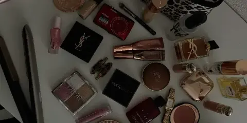 A flat-lay photograph of various professional makeup products, including palettes, foundations, and brushes, alongside a hair straightener.