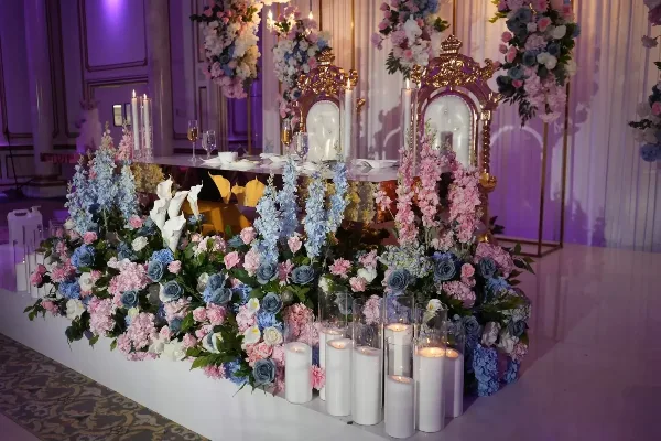 Luxury wedding reception table setting with elaborate floral arrangements, candles, and ornate gold chairs.