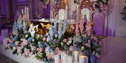 Luxury wedding reception table setting with elaborate floral arrangements, candles, and ornate gold chairs.