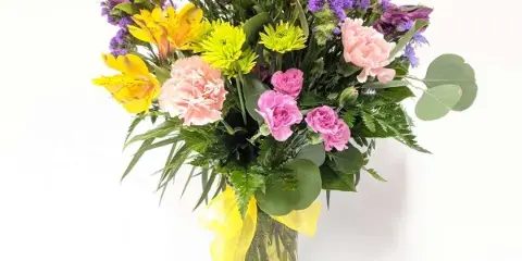A vibrant mixed bouquet of yellow, pink, and purple flowers arranged in a glass vase.