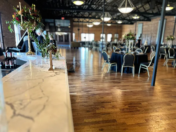 Interior view of a historical ballroom with polished wooden floors, a marble bar, and round tables set for an event.