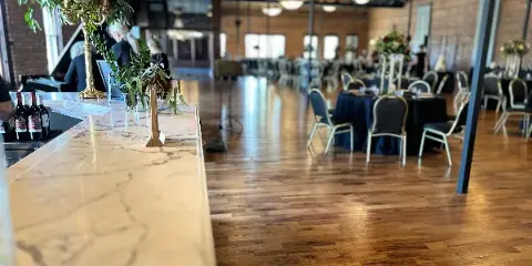 Interior view of a historical ballroom with polished wooden floors, a marble bar, and round tables set for an event.