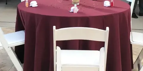 A round event table with a maroon tablecloth, white chairs, and a floral centerpiece.
