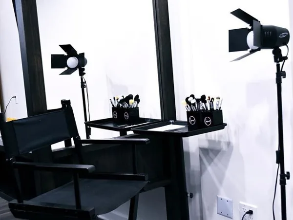 A professional makeup station featuring a director's chair, a large mirror, professional lighting, and makeup brushes.