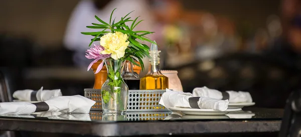 A professionally set catering table featuring white plates, folded napkins, and a floral centerpiece.