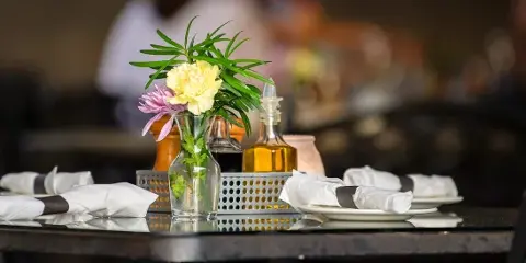 A professionally set catering table featuring white plates, folded napkins, and a floral centerpiece.