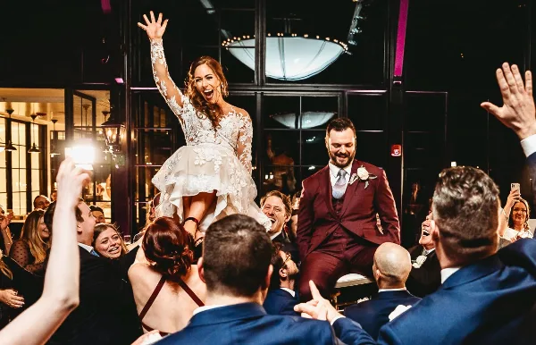 A bride and groom dancing at a wedding reception surrounded by guests.
