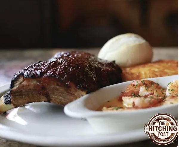 A plated dish featuring a smoked rib, shrimp, and a bread roll served at a restaurant.