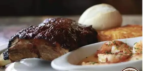 A plated dish featuring a smoked rib, shrimp, and a bread roll served at a restaurant.