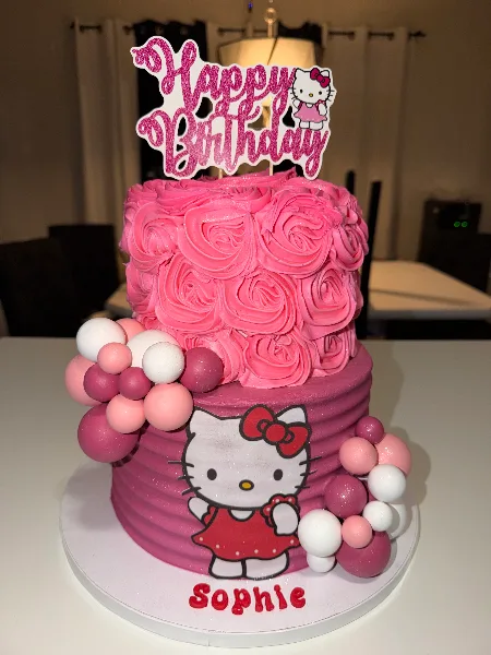 A custom two-tiered pink cake decorated with rosettes, fondant spheres, and a Hello Kitty topper.