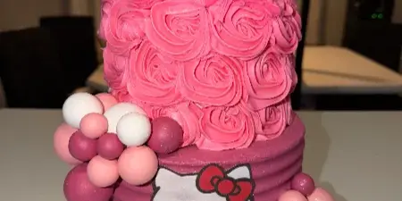 A custom two-tiered pink cake decorated with rosettes, fondant spheres, and a Hello Kitty topper.
