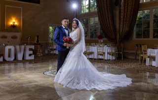 A bride and groom standing in a large indoor wedding venue with a polished dance floor and set tables.