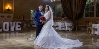 A bride and groom standing in a large indoor wedding venue with a polished dance floor and set tables.