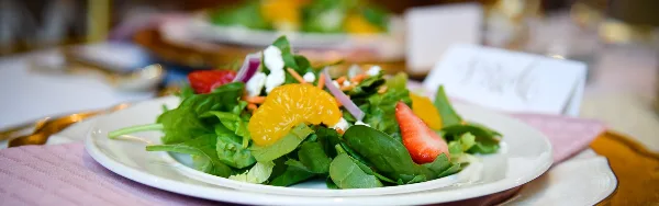 A plated fresh salad with greens, strawberries, orange slices, and cheese on a white plate at a set event table.