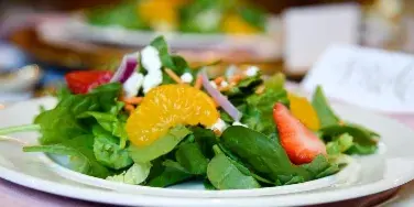 A plated fresh salad with greens, strawberries, orange slices, and cheese on a white plate at a set event table.