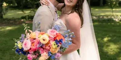 A bride and groom embracing outdoors, with the bride holding a colorful bouquet of flowers.