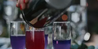 A bartender pouring a colorful cocktail from a shaker into a champagne flute at an outdoor event.