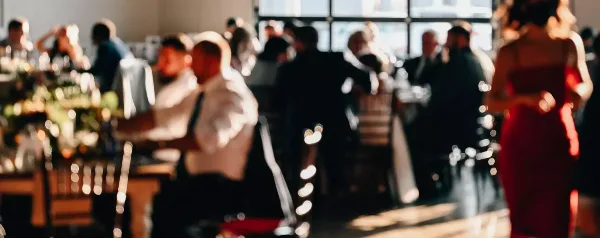 A server in a white shirt and suspenders attends to guests at a formal event with tables and floral arrangements.