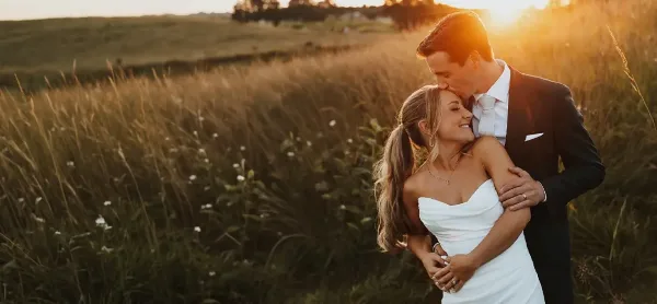 A bride and groom embracing in a field of tall grass during golden hour.
