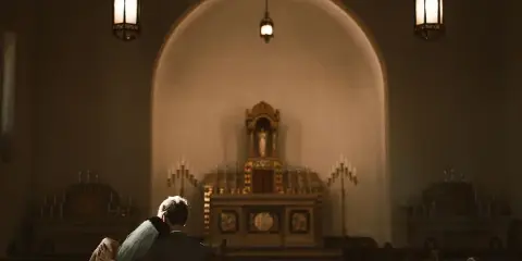 A cinematic photograph of a couple embracing in a church pew, facing an ornate altar with warm lighting.