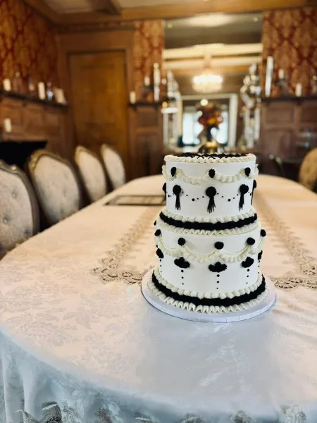 A three-tier white wedding cake with black fondant decorations and ruffles sitting on a table in a formal dining room.