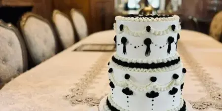 A three-tier white wedding cake with black fondant decorations and ruffles sitting on a table in a formal dining room.