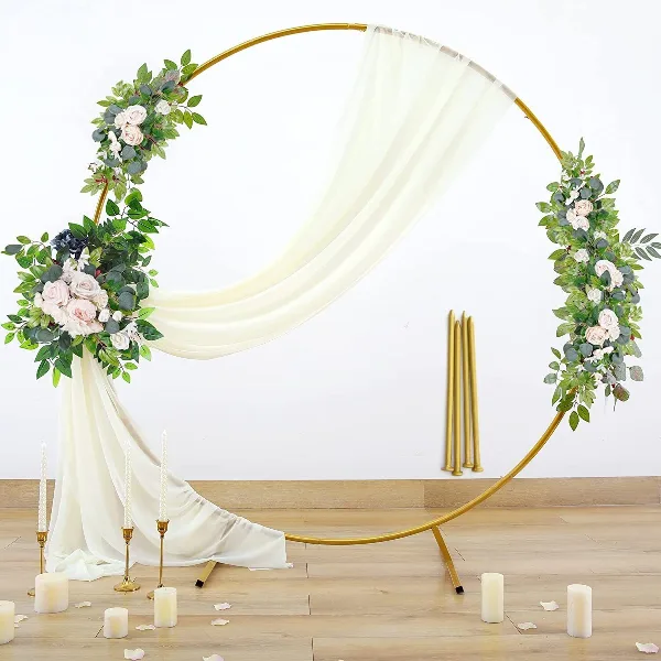 A golden circular wedding arch decorated with floral arrangements and white drapery.