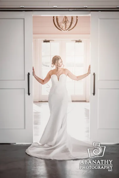 A bride in a white wedding dress standing in a doorway with her arms outstretched.
