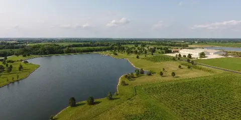 Aerial view of the Bourgmont Winery estate featuring vineyard rows, a large pond, and the main winery buildings.