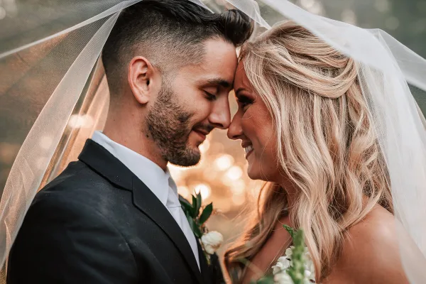 Bride and groom smiling face-to-face under a wedding veil