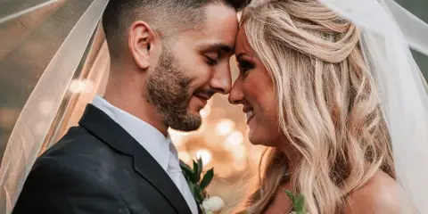 Bride and groom smiling face-to-face under a wedding veil