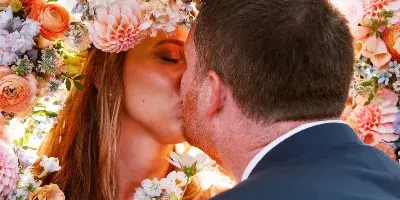 A bride and groom kissing at a wedding ceremony under a large floral arch.