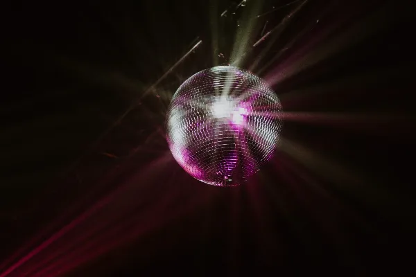 A disco ball reflecting purple and white light beams in a dark room.