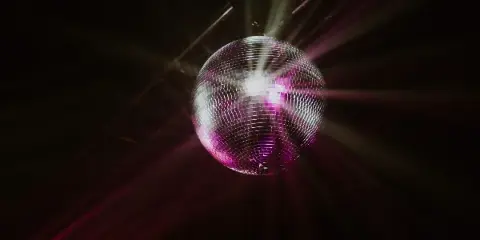 A disco ball reflecting purple and white light beams in a dark room.