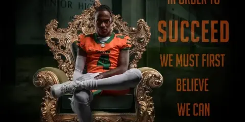 A high school football player in an orange jersey sitting on an ornate gold chair in a studio setting.