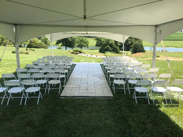 A white event tent set up on a grassy field with rows of white folding chairs arranged for a ceremony.
