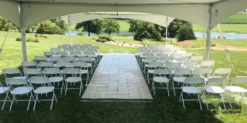 A white event tent set up on a grassy field with rows of white folding chairs arranged for a ceremony.