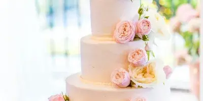 A four-tier white wedding cake decorated with cascading pink and cream roses, displayed on a silver stand.