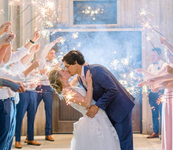 A bride and groom kissing during a sparkler exit at a rustic wedding venue.