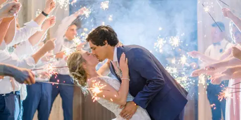 A bride and groom kissing during a sparkler exit at a rustic wedding venue.