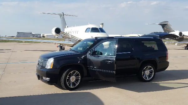 A black luxury SUV parked on an airport tarmac with a private jet in the background.